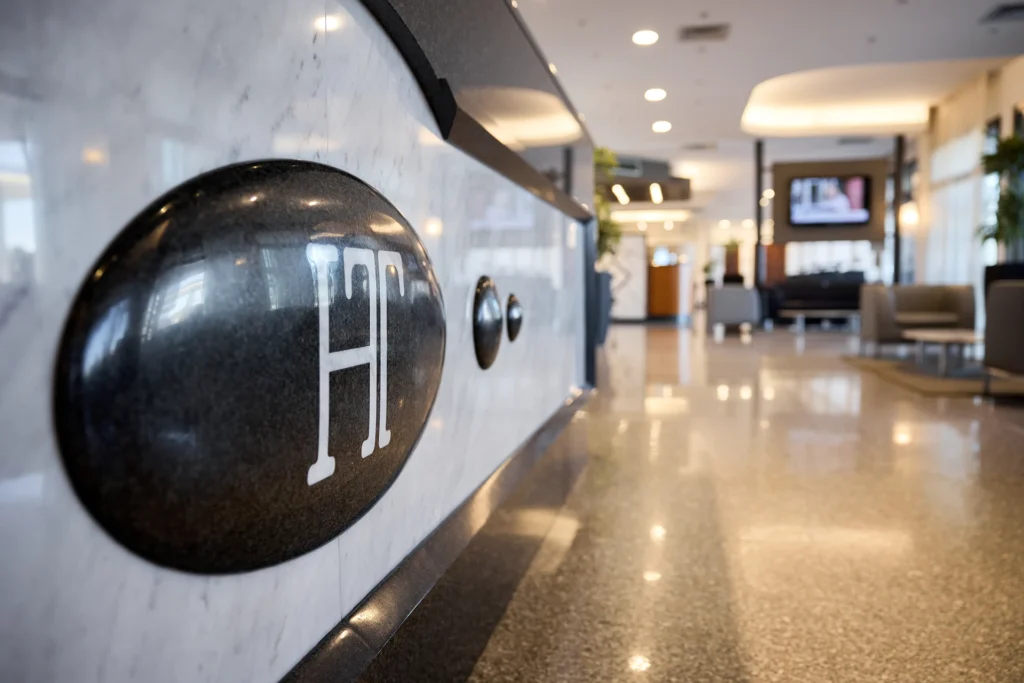 Hotel lobby, with detail of the reception desk in the foreground and lounge with sofas and armchairs in the background.